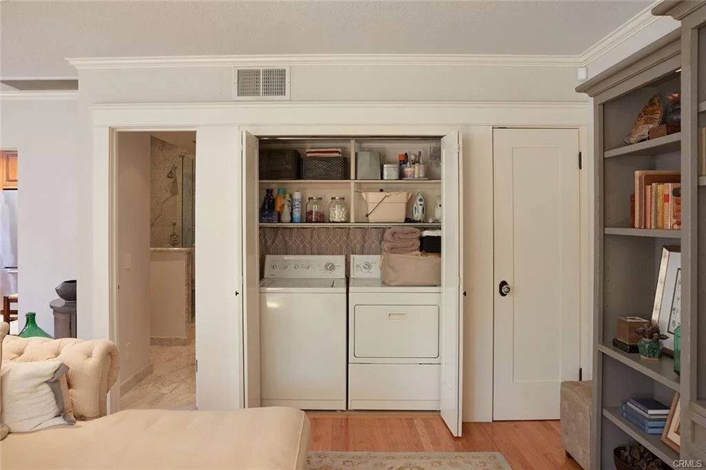 Laundry closet with stacked washer and dryer, shelves, and cleaning supplies.