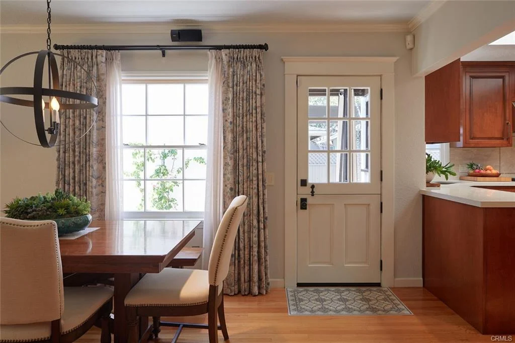 Dining area with table, chairs, window with curtains, door, and kitchen cabinets.
