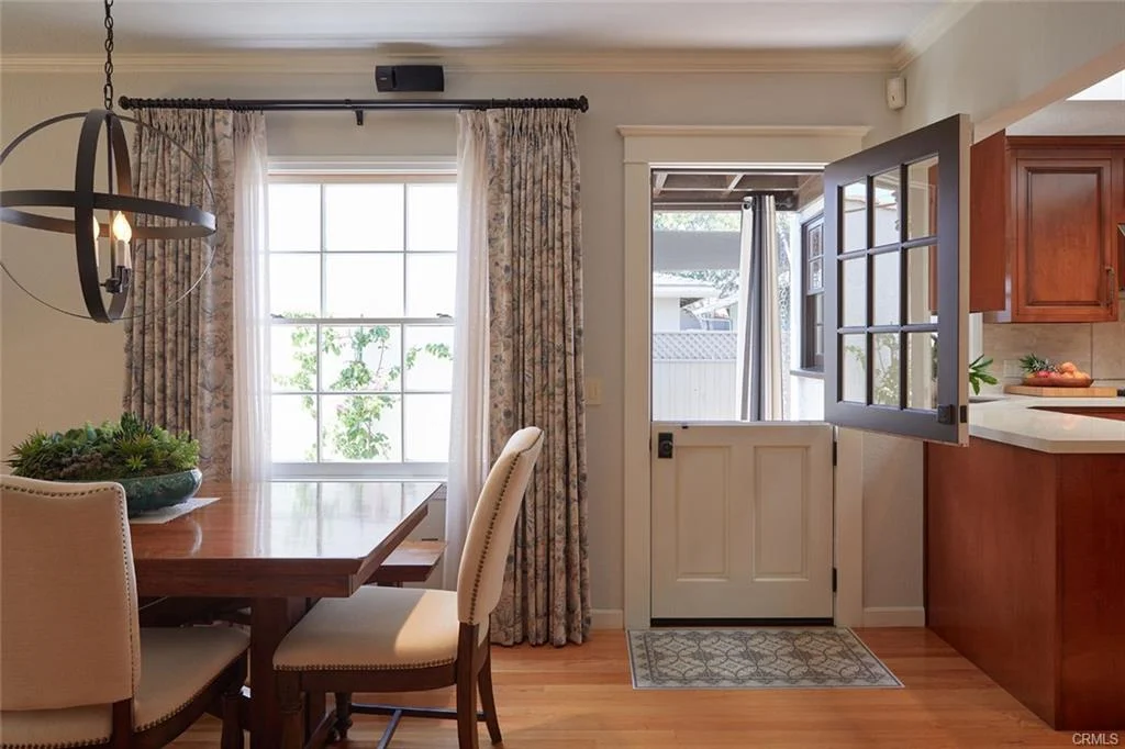 Dining area with wooden table, chairs, window with curtains, and open door.