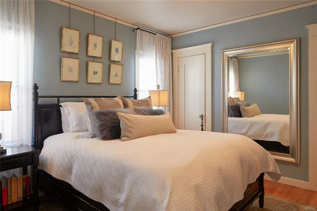Bedroom with bed, pillows, bedside lamps, mirror, and light blue walls with artwork.