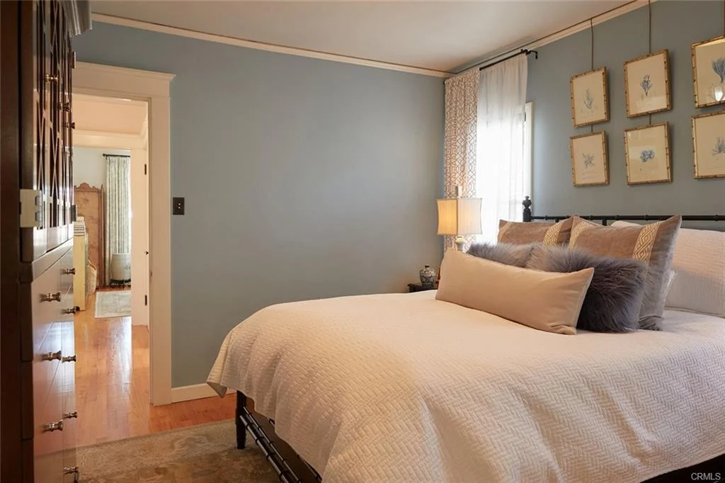 Cozy bedroom with bed, pillows, light blue walls, and framed artwork.