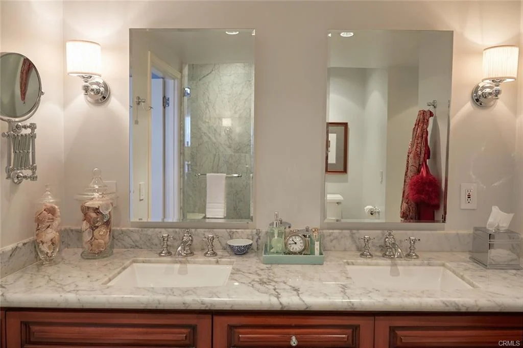 Bathroom with double vanity, marble countertop, two sinks, mirrors, and decor items.