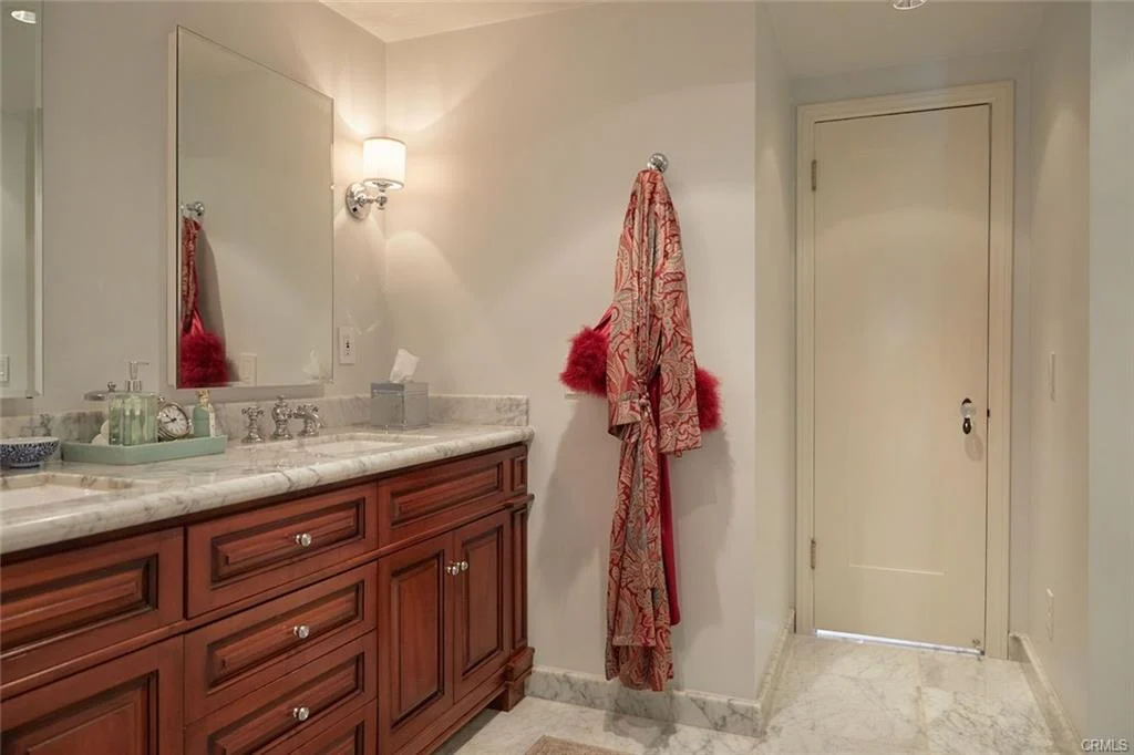Bathroom with double vanity, wooden cabinets, marble countertop, two mirrors, and red robe.