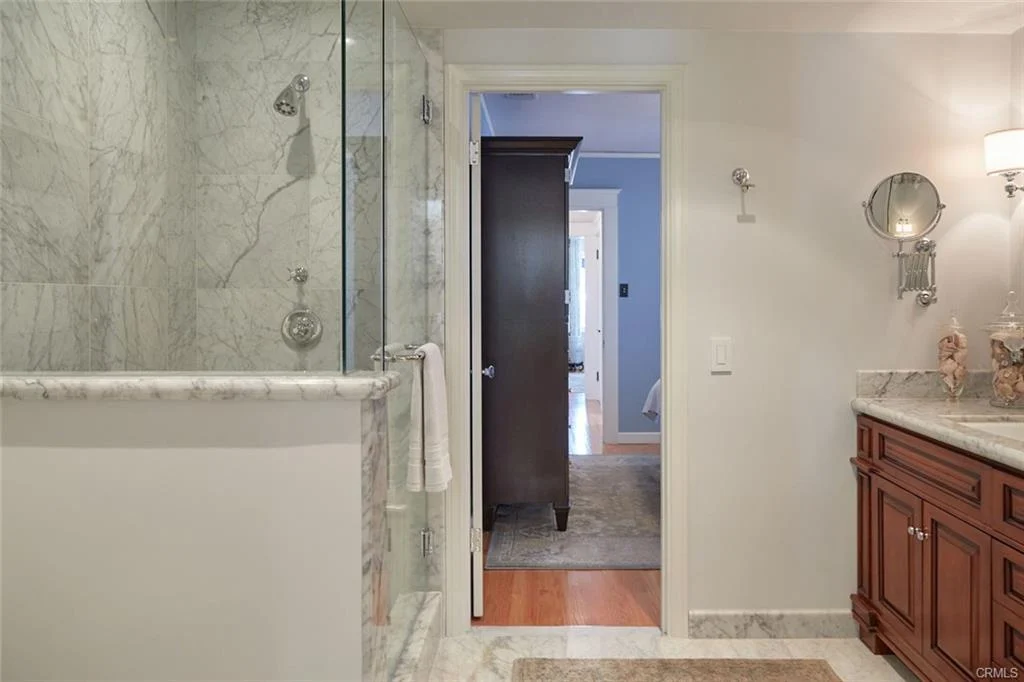 Bathroom with glass shower, marble walls, and wooden vanity with sink.