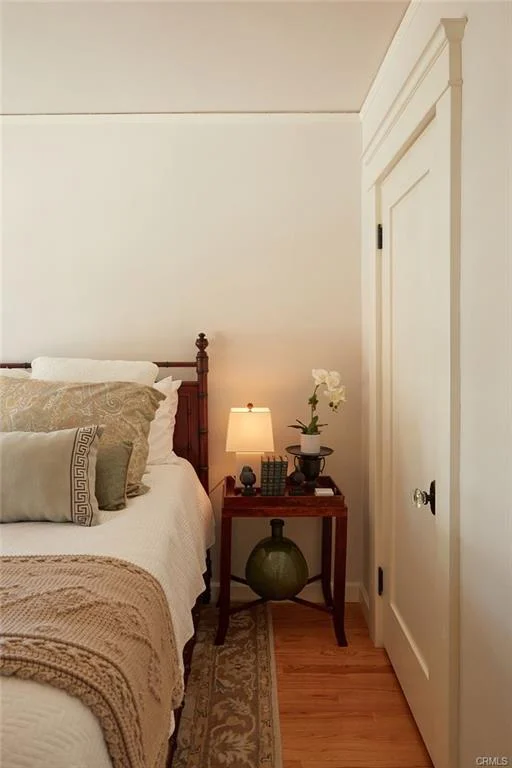 Bedroom corner with bed, nightstand, lamp, orchid plant, and door.