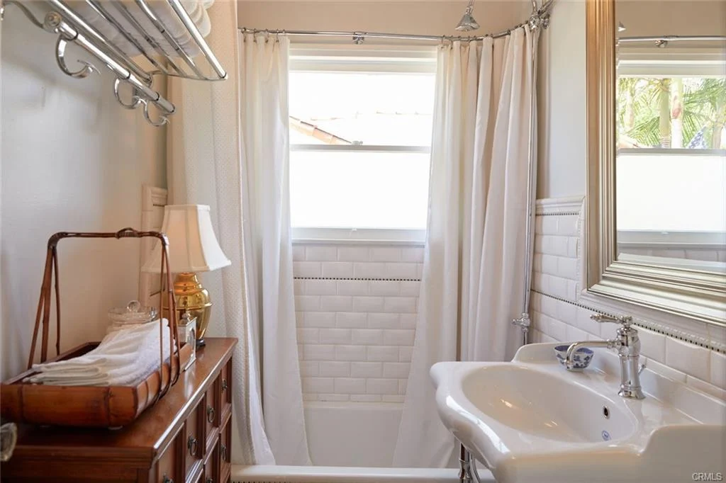 Small bathroom with a white tub, shower curtain, sink with vintage faucet, and wooden towel storage.