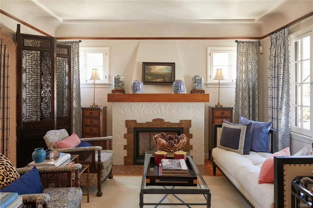 Living room with fireplace, couch, chairs, pillows, wall art, and curtains