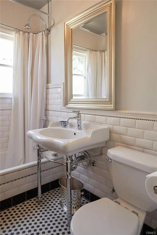 Bathroom with a shower, white curtain, sink on chrome stand, toilet, black and white tile floor, and a mirror.