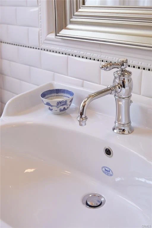 Close-up of a sink with a chrome faucet, white tile wall, and a small blue and white bowl.