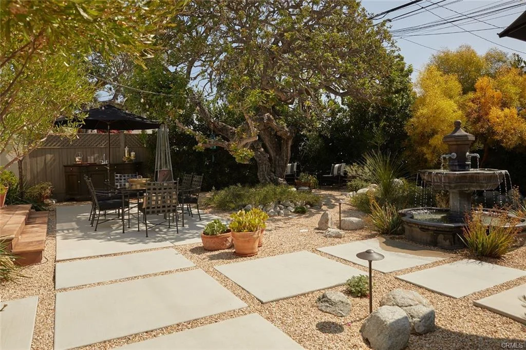Backyard with stone patio, table, chairs, plants, fountain, and colorful trees