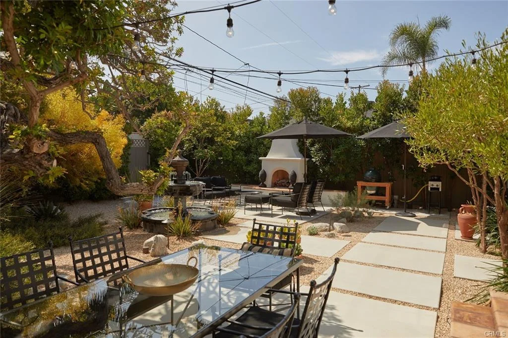 Garden with table, chairs, umbrellas, stone path, plants, fountain, and fireplace