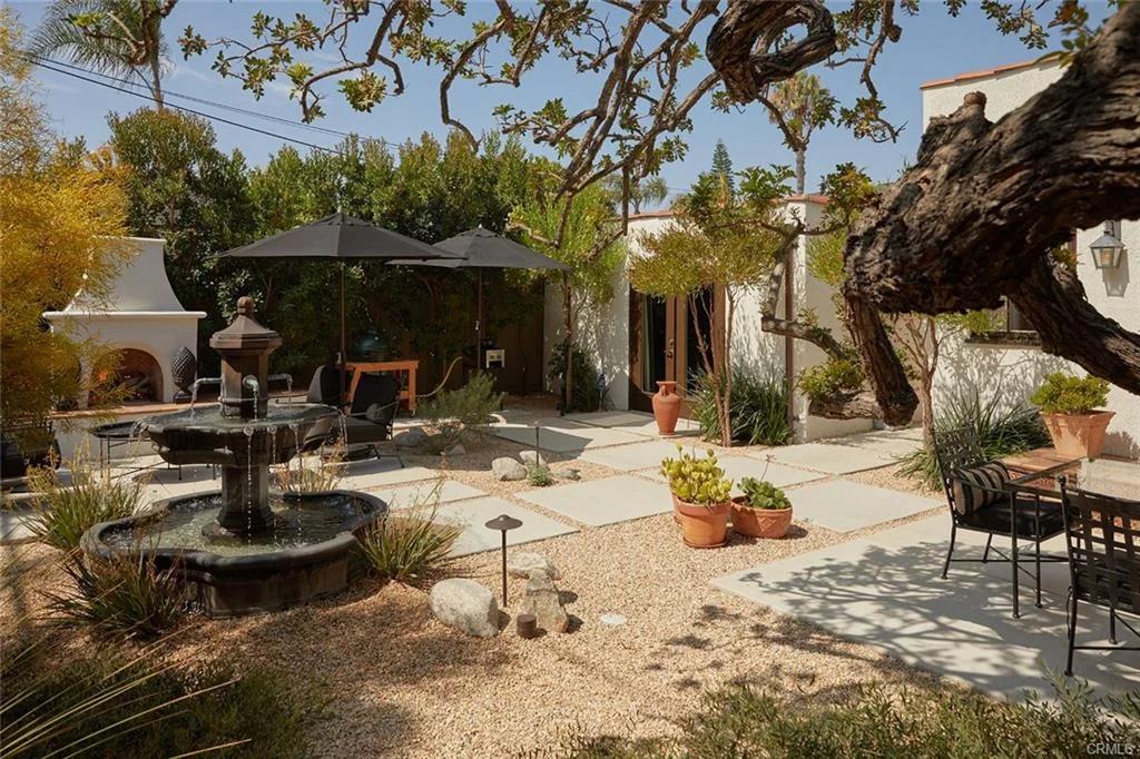 Garden with stone fountain, plants, patio furniture, umbrella, and gravel path