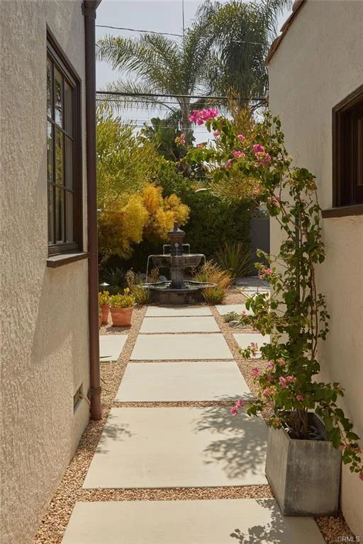 Narrow walkway with plants leading to garden fountain