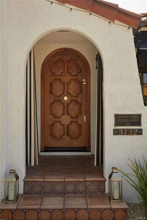 Wooden door with ornate design, stucco arch, lanterns, and house number 3722