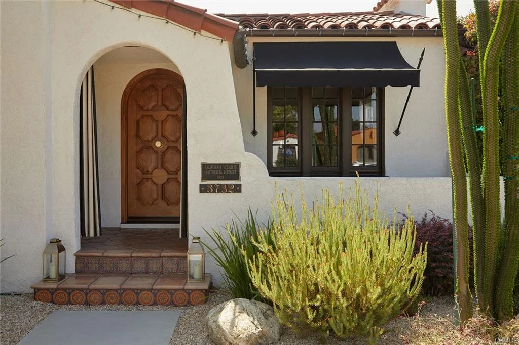 House in California real estate with stucco walls, tile roof, arched door, and plants
