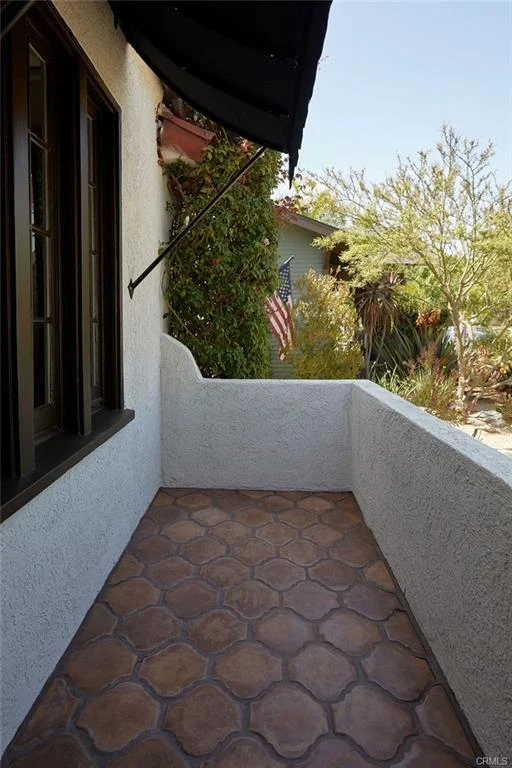Balcony with tiled floor, plants, white wall, and flag