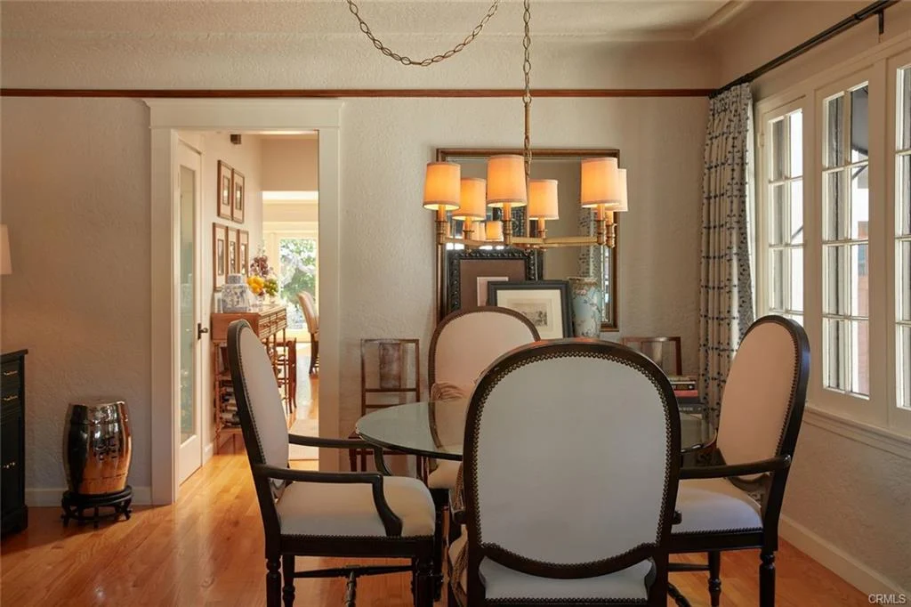 Dining room with round glass table, chairs, chandelier, and window curtains