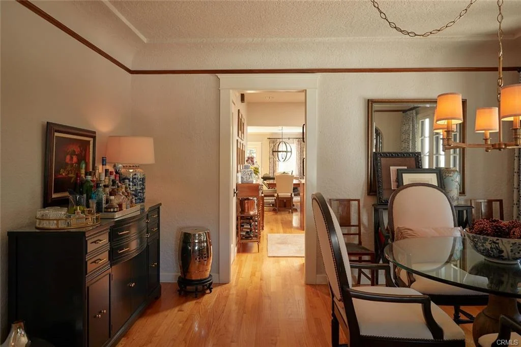 Dining area with glass table, chairs, sideboard, wooden floor, and light fixtures.