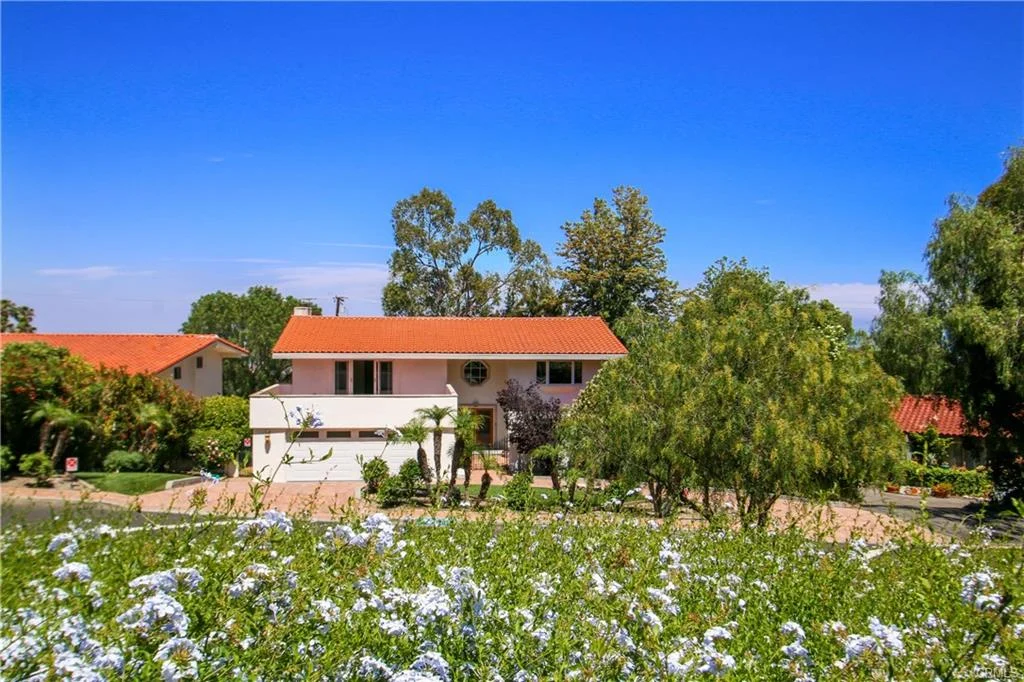 Two-story house with red-tiled roof and plants, California real estate.