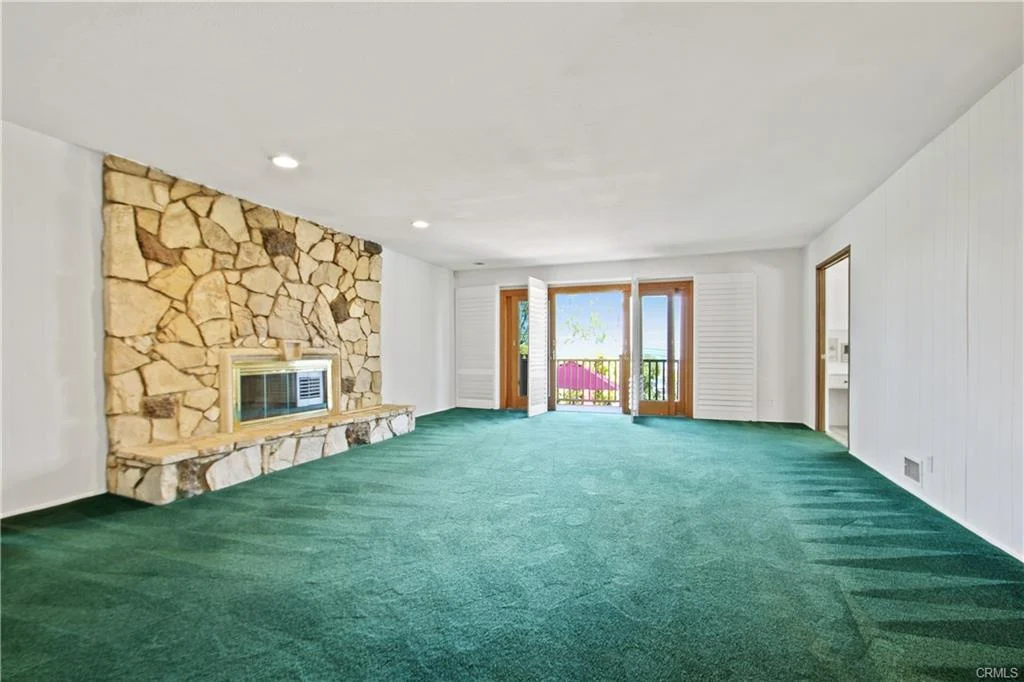 Living room with green carpet, stone fireplace, and windows.