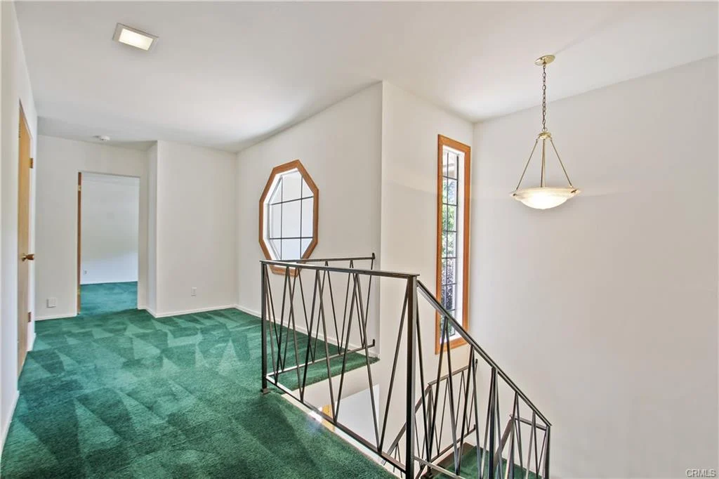 Hallway with green carpet, staircase, and windows.