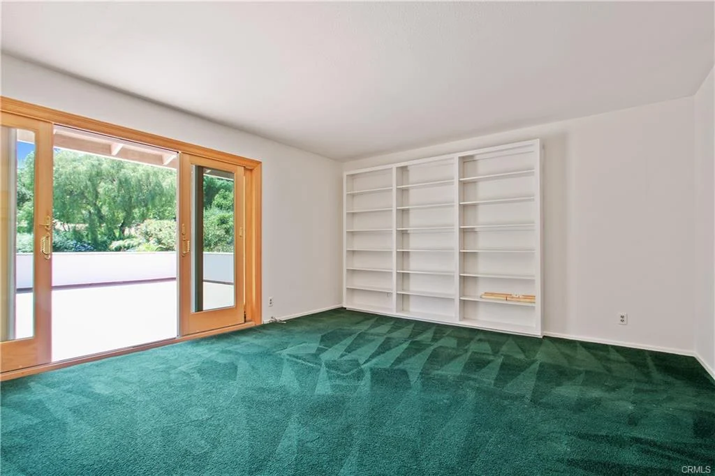 Room with green carpet, sliding doors, and bookshelf.