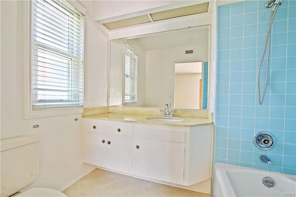Bathroom with sink, mirror, cabinet, and blue tiled wall.