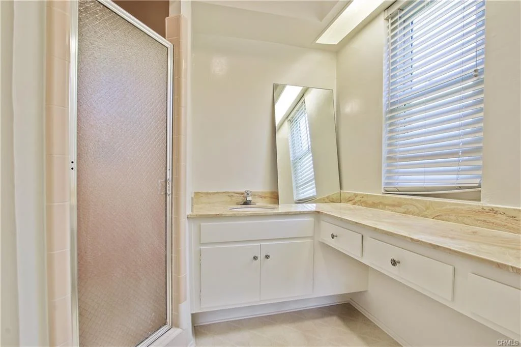 Bathroom with glass shower, sink, mirror, and window.
