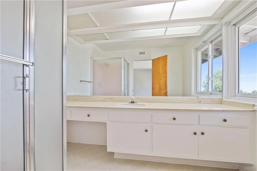Bathroom with vanity, mirror, windows, and shower.