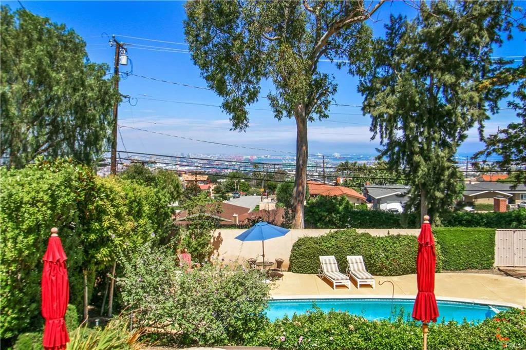 Backyard with swimming pool, loungers, umbrellas, and houses, California real estate.