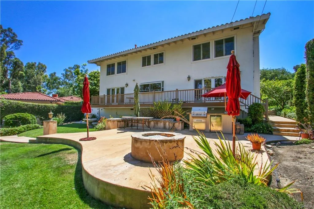Two-story house with balcony, fire pit, plants, and umbrellas, California real estate.