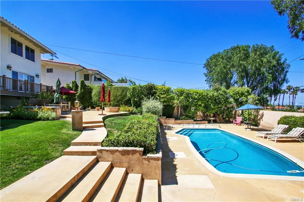 Backyard with swimming pool, lounge chairs, plants, and house, California real estate.