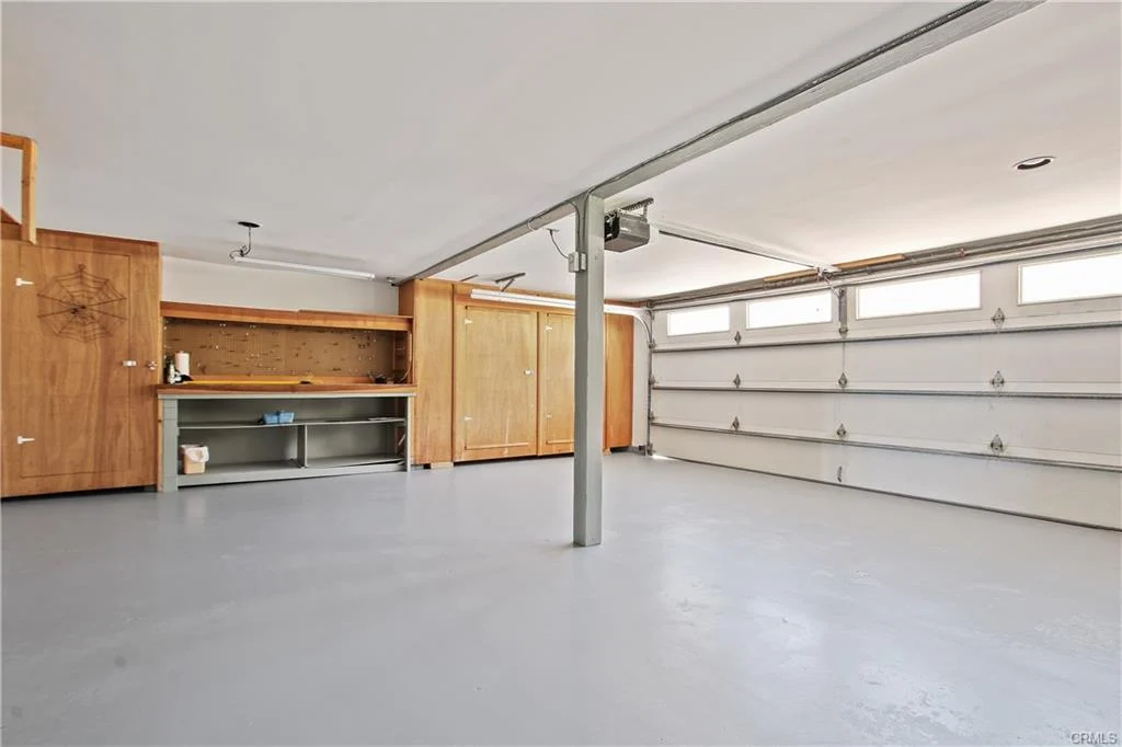 Garage with concrete floor, wooden cabinets, and large door.