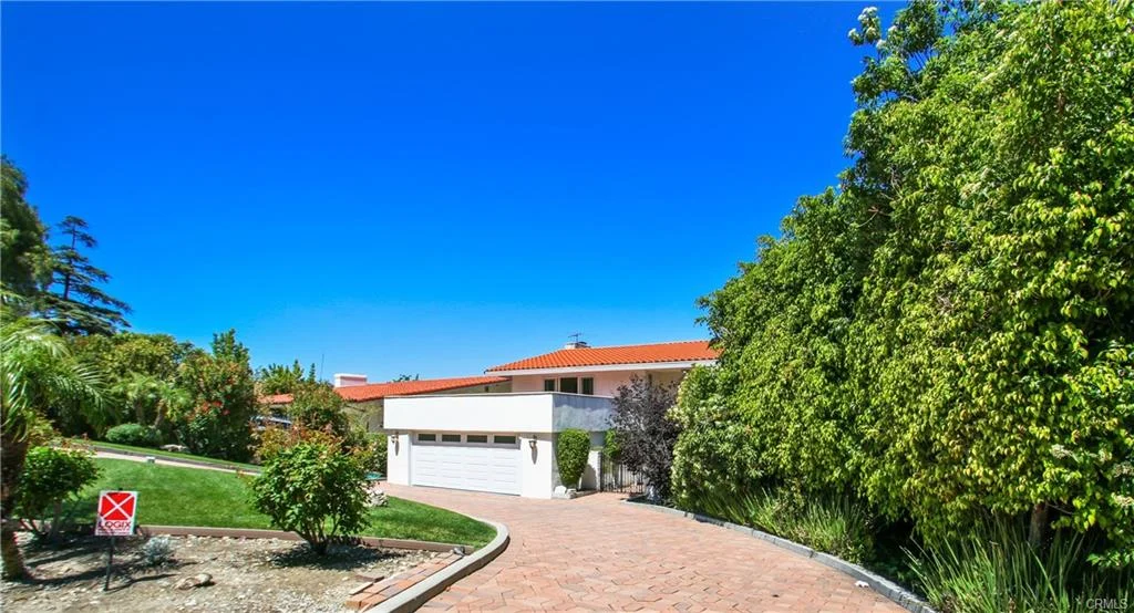Modern house with red tile roof, driveway, and plants, California real estate.