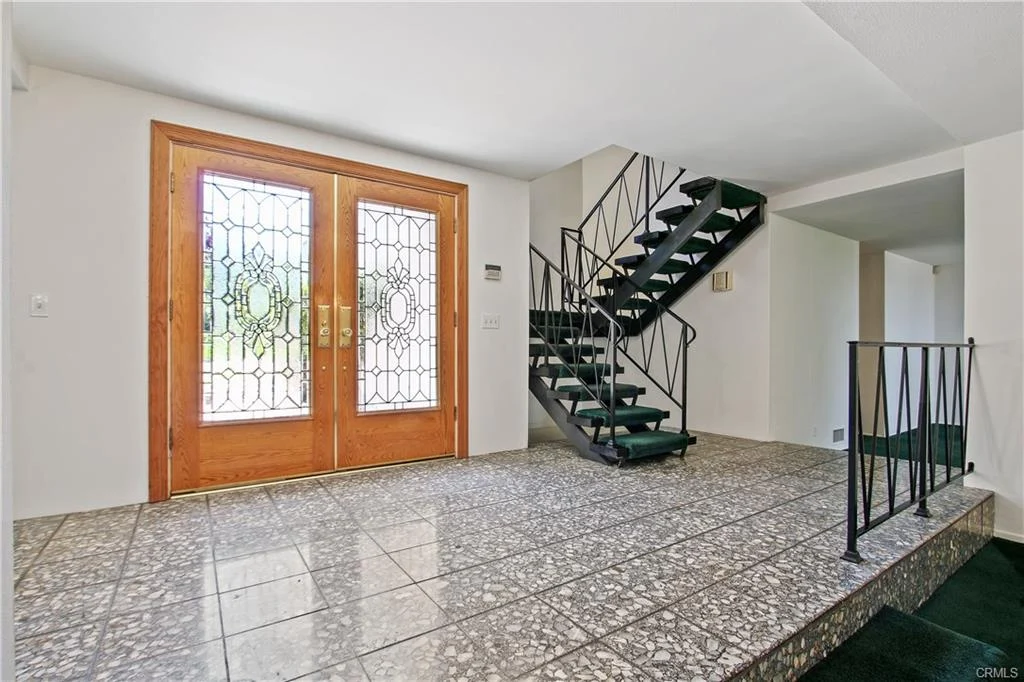 Entryway with double wooden doors, glass panels, staircase, and tiled floor.
