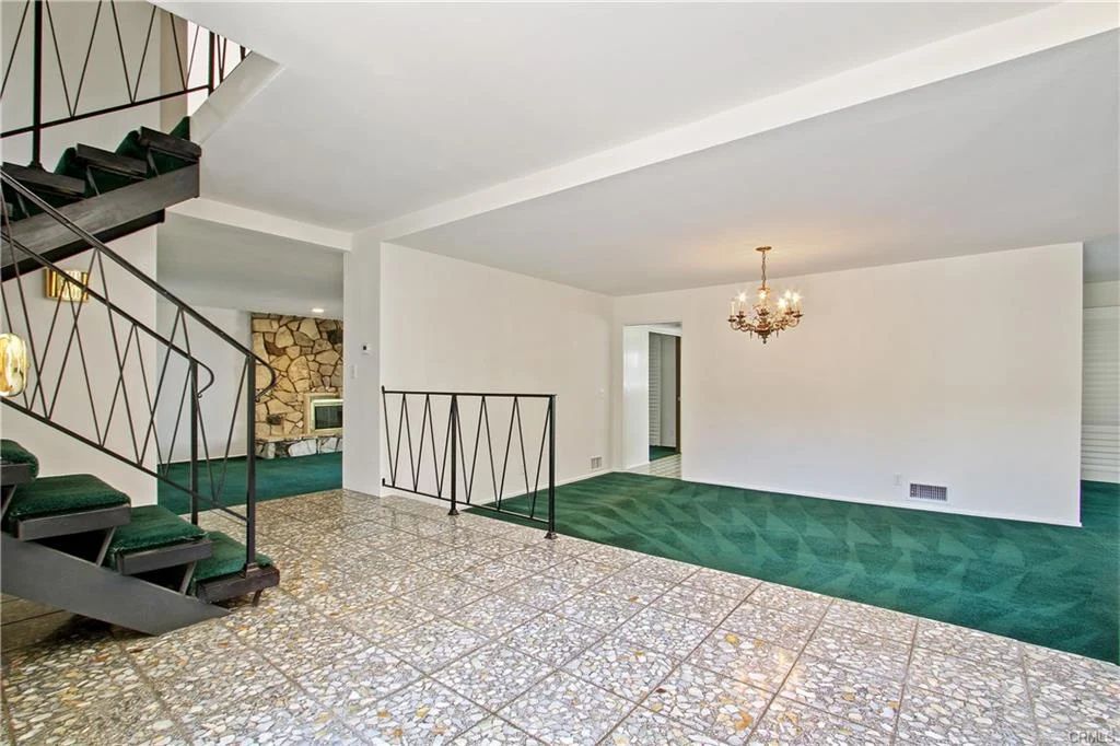 Interior of house with green carpet, staircase, chandelier, and stone wall, California real estate.