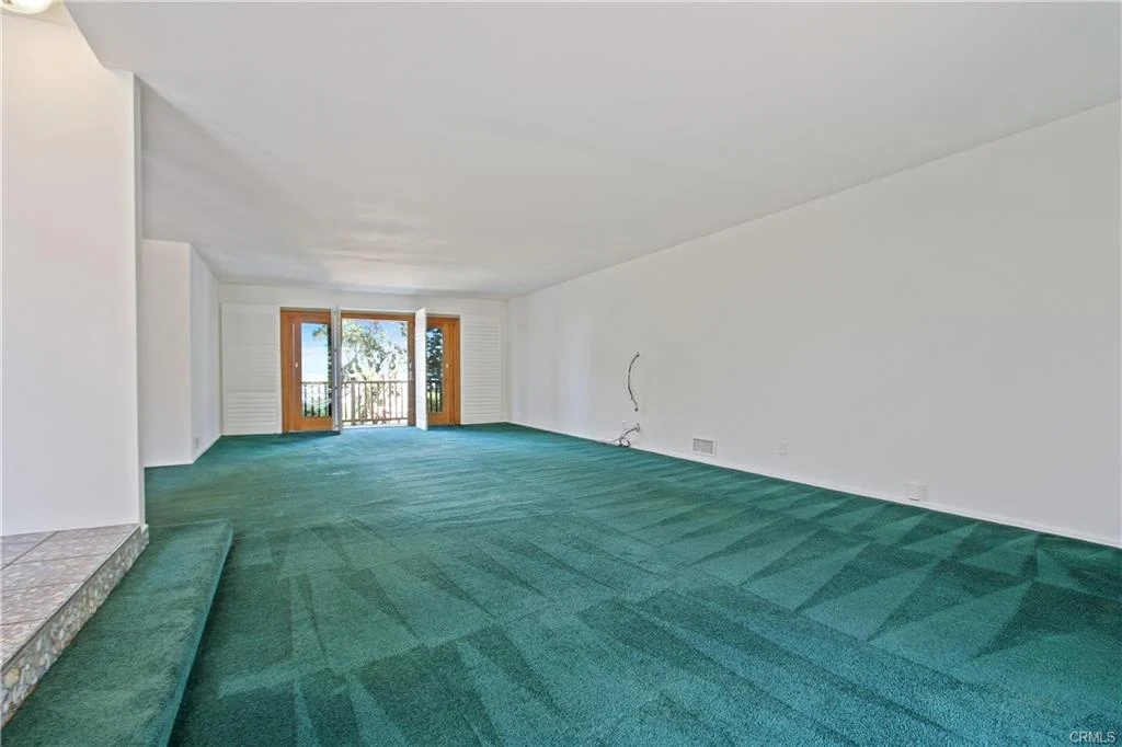 Room with green carpet, white walls, and windows.