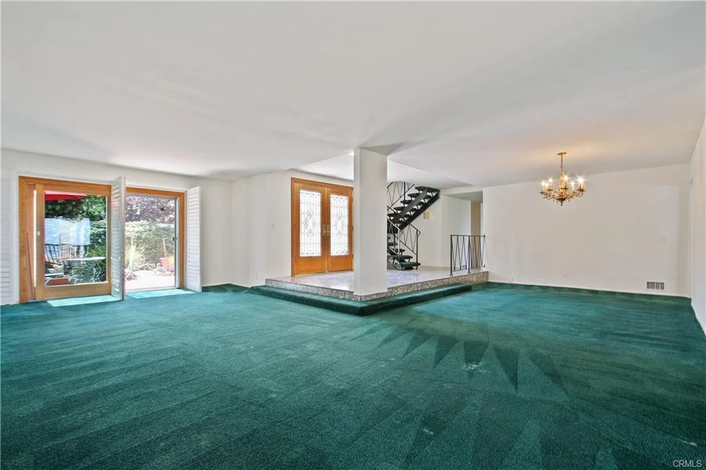 Living room with green carpet, windows, and staircase.