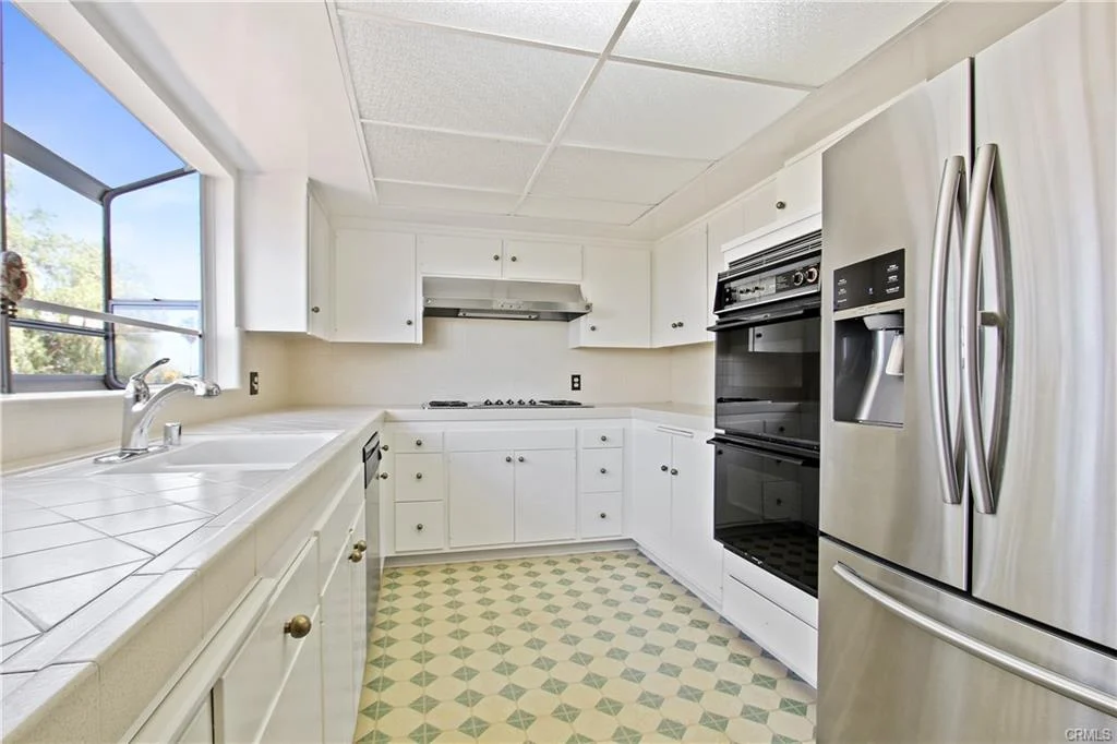 Kitchen with white cabinets, refrigerator, oven, stovetop, and window.