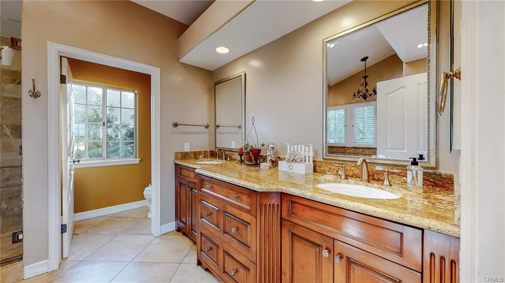 Bathroom with double vanity, wooden cabinets, mirror, window, and toilet