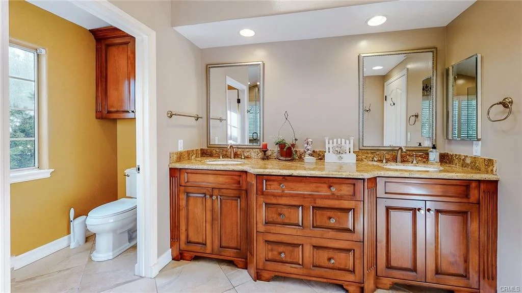 Bathroom with double sink, wooden cabinets, mirrors, and toilet
