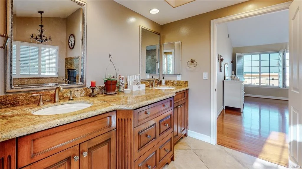 Bathroom with dual sinks, wooden cabinets, granite countertops, mirror, and window