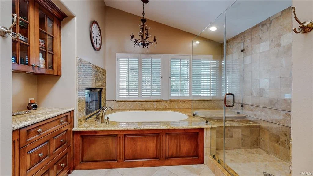 Luxury bathroom with soaking tub, glass shower, wooden cabinets, and windows