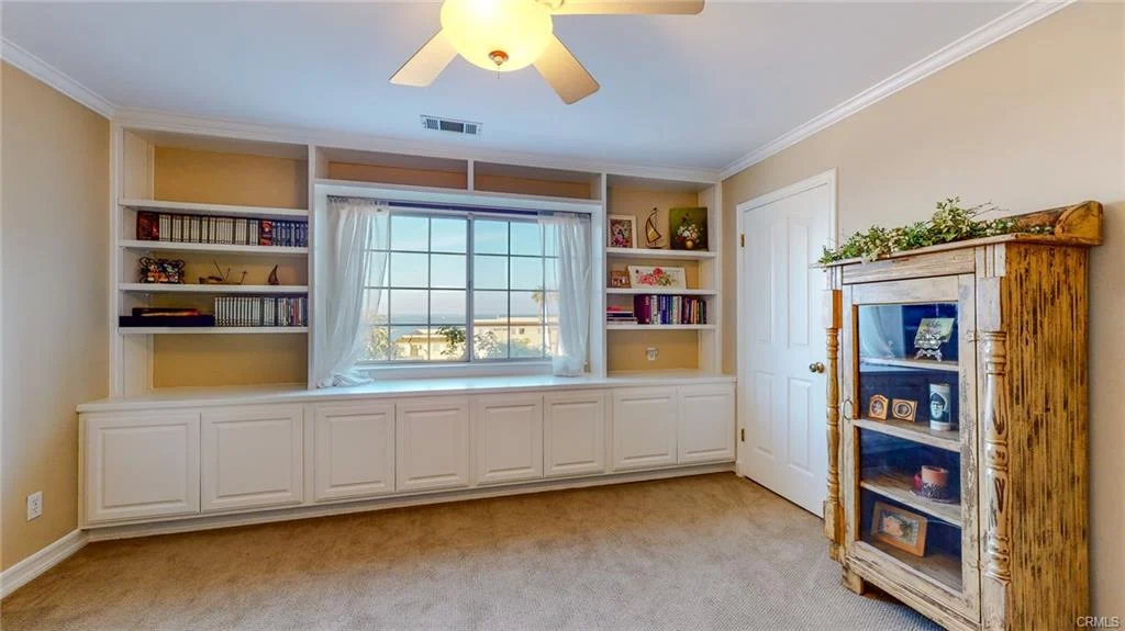 Bedroom with large window, built-in shelves, wooden cabinet, and carpet