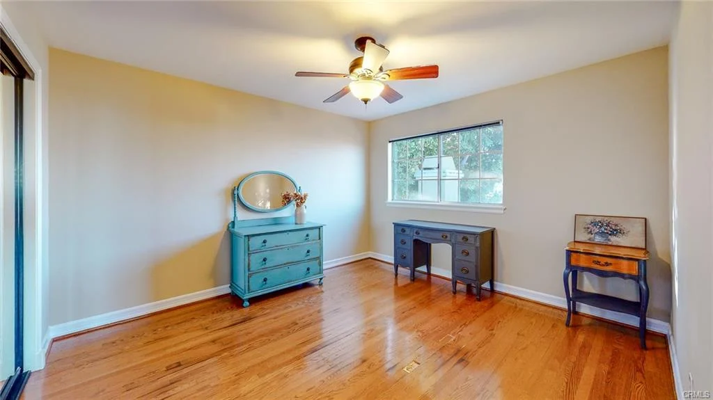 Room with hardwood floor, ceiling fan, blue dresser, desk, and window