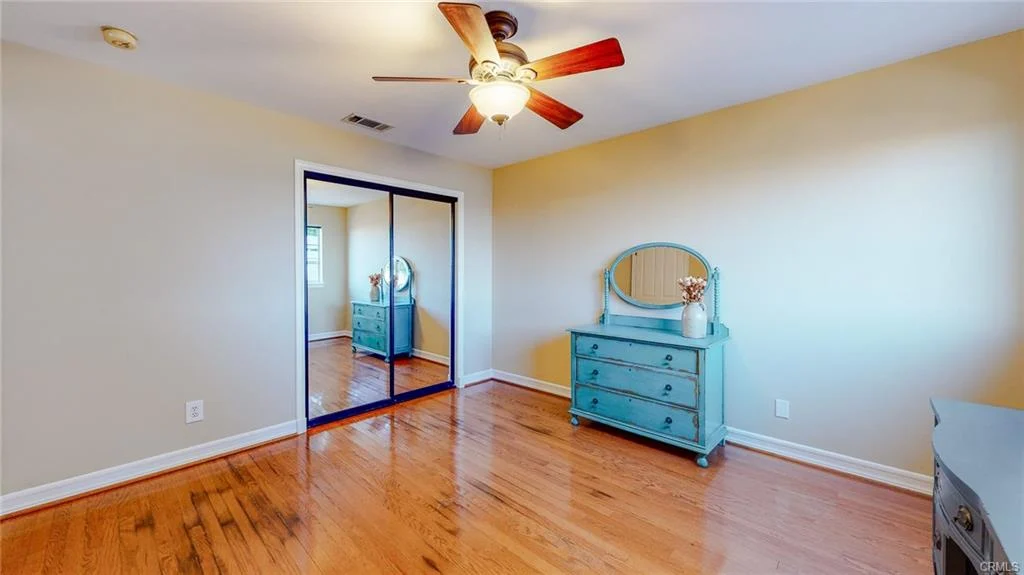 Room with wooden floor, ceiling fan, dresser, mirror, and mirrored closet