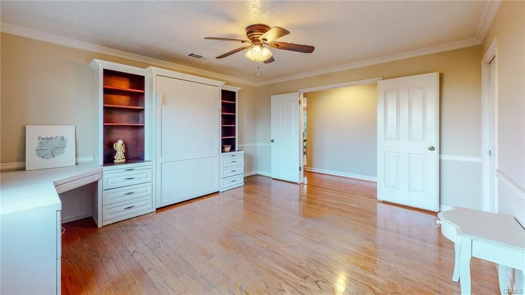 Spacious room with hardwood floor, ceiling fan, built-in shelves, and white cabinets
