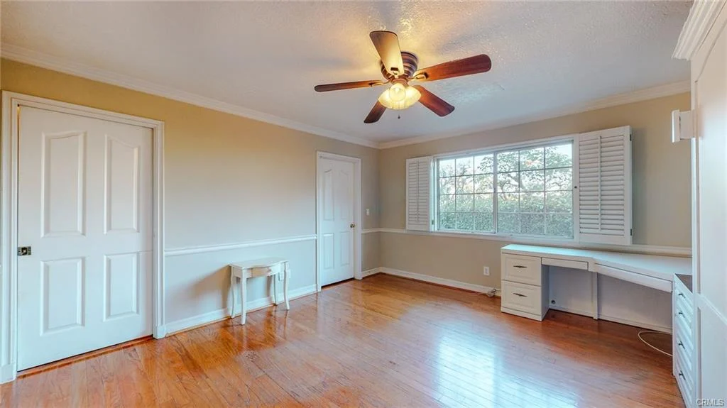 Empty room with wooden floor, ceiling fan, window, chair, and built-in desk
