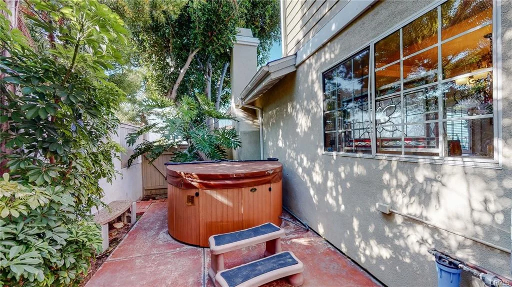 Patio with hot tub, greenery, and bench