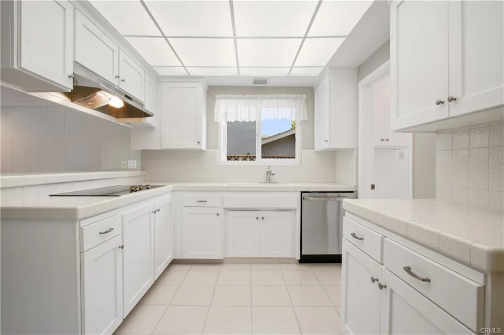 Bright white kitchen with a sink and stainless steel appliances.